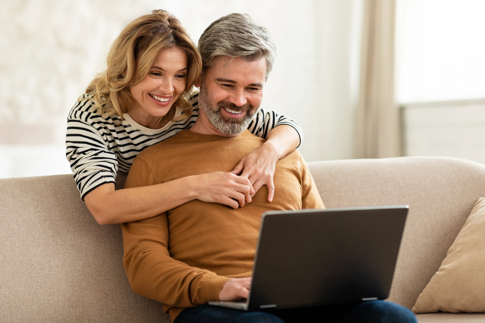 Consultation financière à domicile entre un conseiller et un couple de seniors assis sur canapé bleu